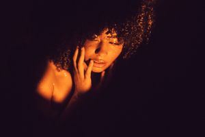 Artistic portrait illuminated by warm orange light against dark background creating dramatic shadows and contrast.