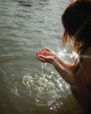 Someone's hands creating mesmerizing sparkles in dark rippling water at twilight.