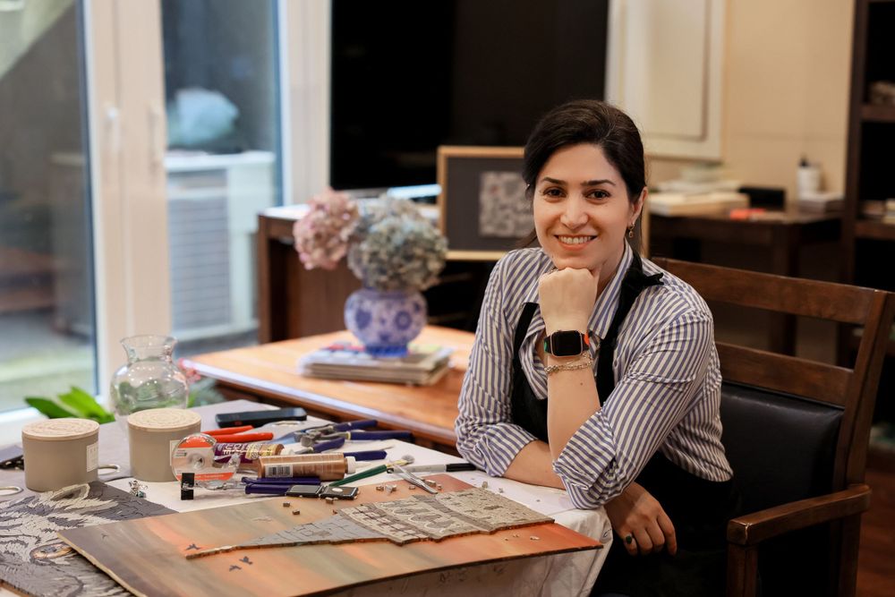 Person working at a wooden table with crafting supplies and coffee laid out in a well-lit room.
