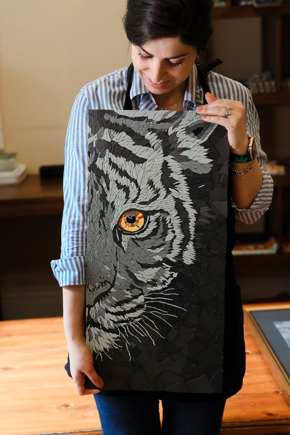 Someone wearing a striped shirt shows off their artwork featuring a detailed black and gray tiger face on dark fabric.
