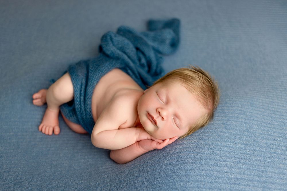 Peaceful sleeping newborn swaddled in soft blue fabric on textured blue background for infant portrait photography.
