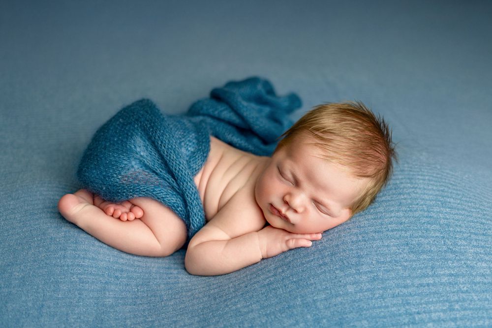 Peaceful sleeping newborn baby wrapped in soft turquoise fabric lying on textured blue blanket.