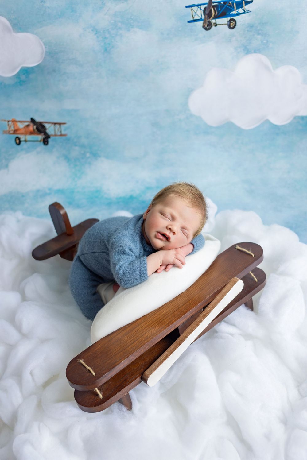 Sweet newborn photography setup with toy wooden airplane, soft cloud backdrop and vintage biplane decorations in the sky.