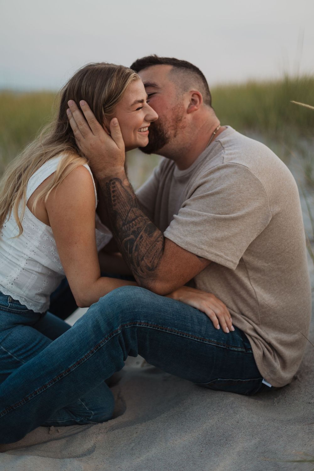 Affectionate couple sharing an intimate moment outdoors while sitting together on a sandy surface at sunset.