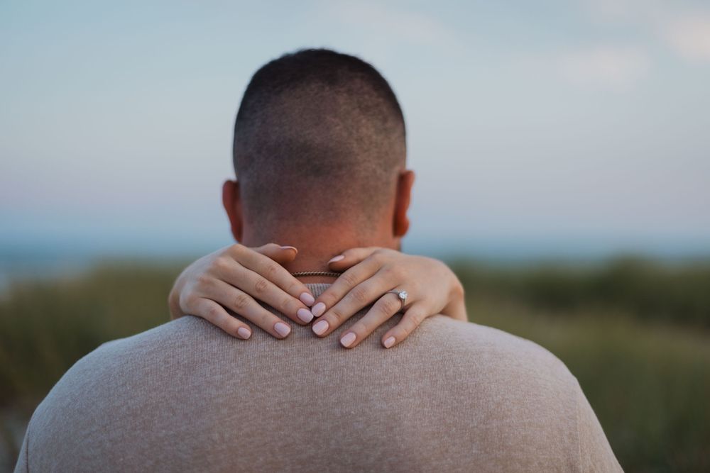 Close-up view of hands resting on back of head against blurred natural outdoor background.