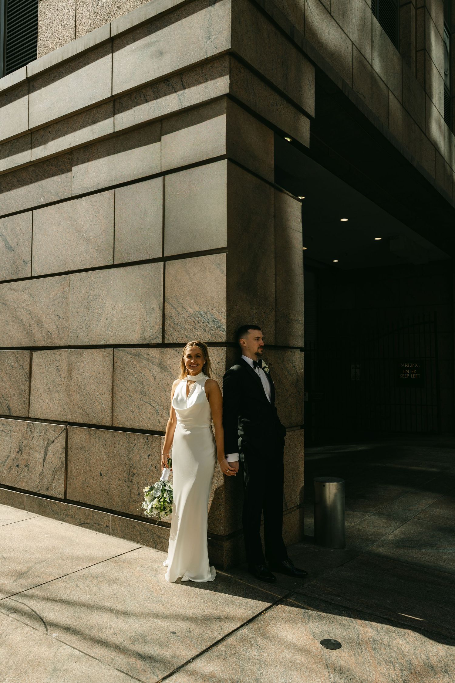 Modern wedding portrait against stone building in downtown setting.