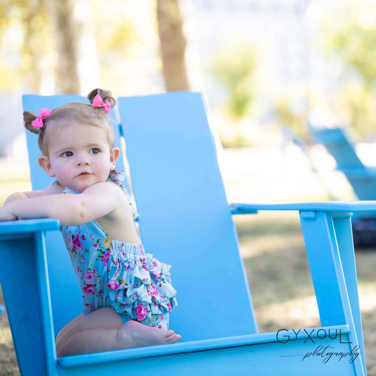 Small child in floral outfit sitting on bright blue lounge chair outdoors.