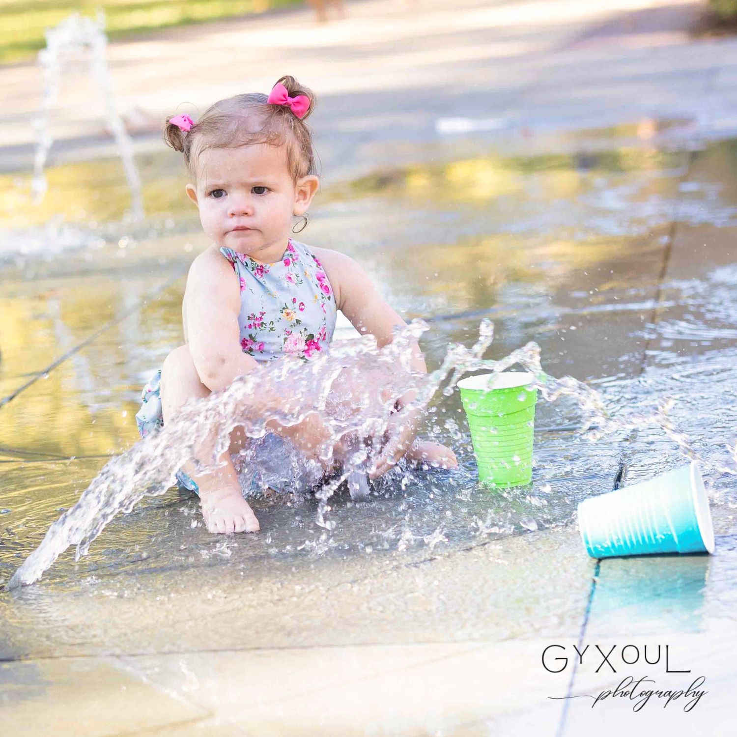 Child in floral swimsuit playing and splashing in water with colorful cups.