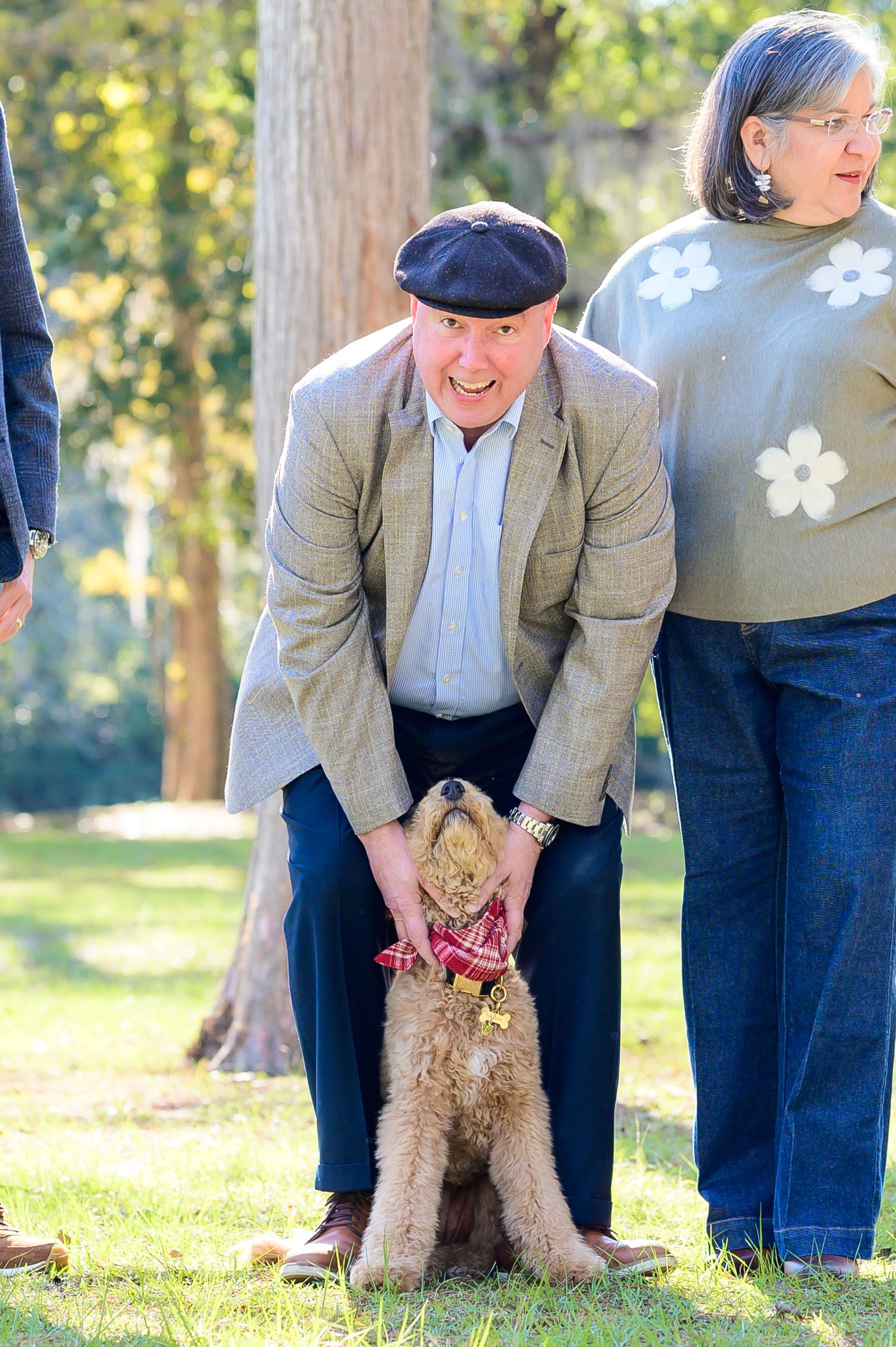 A small fluffy dog poses with people in casual attire outdoors on a sunny day.