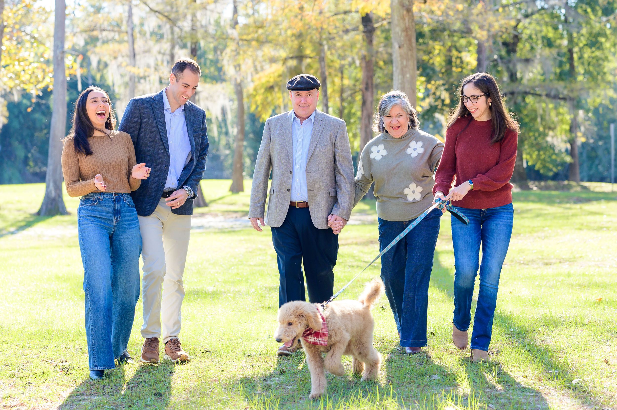 Group portrait of people and a small dog walking together on grass in casual fall attire.
