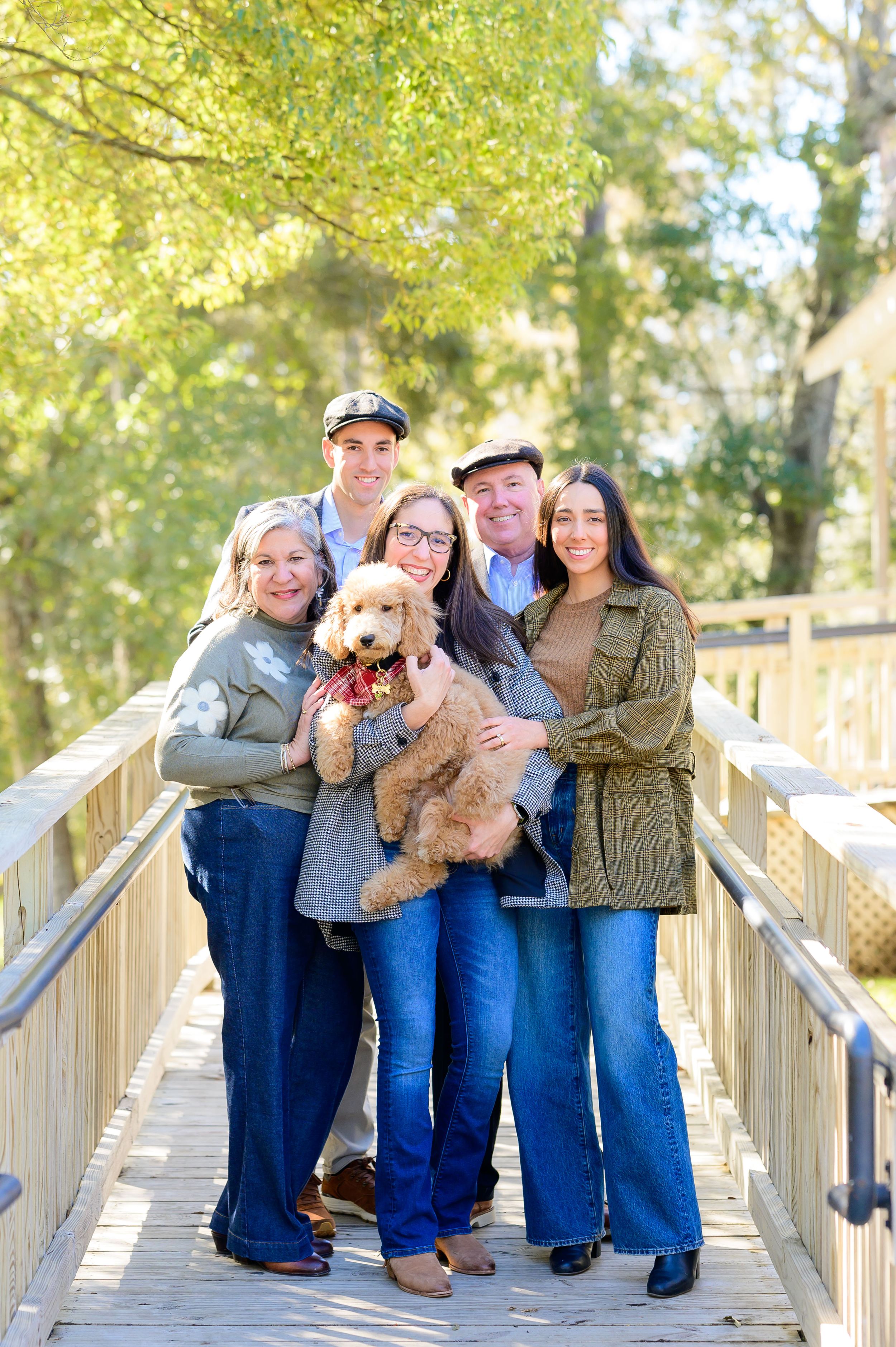 Family group poses with their fluffy dog on a wooden boardwalk surrounded by fall foliage.
