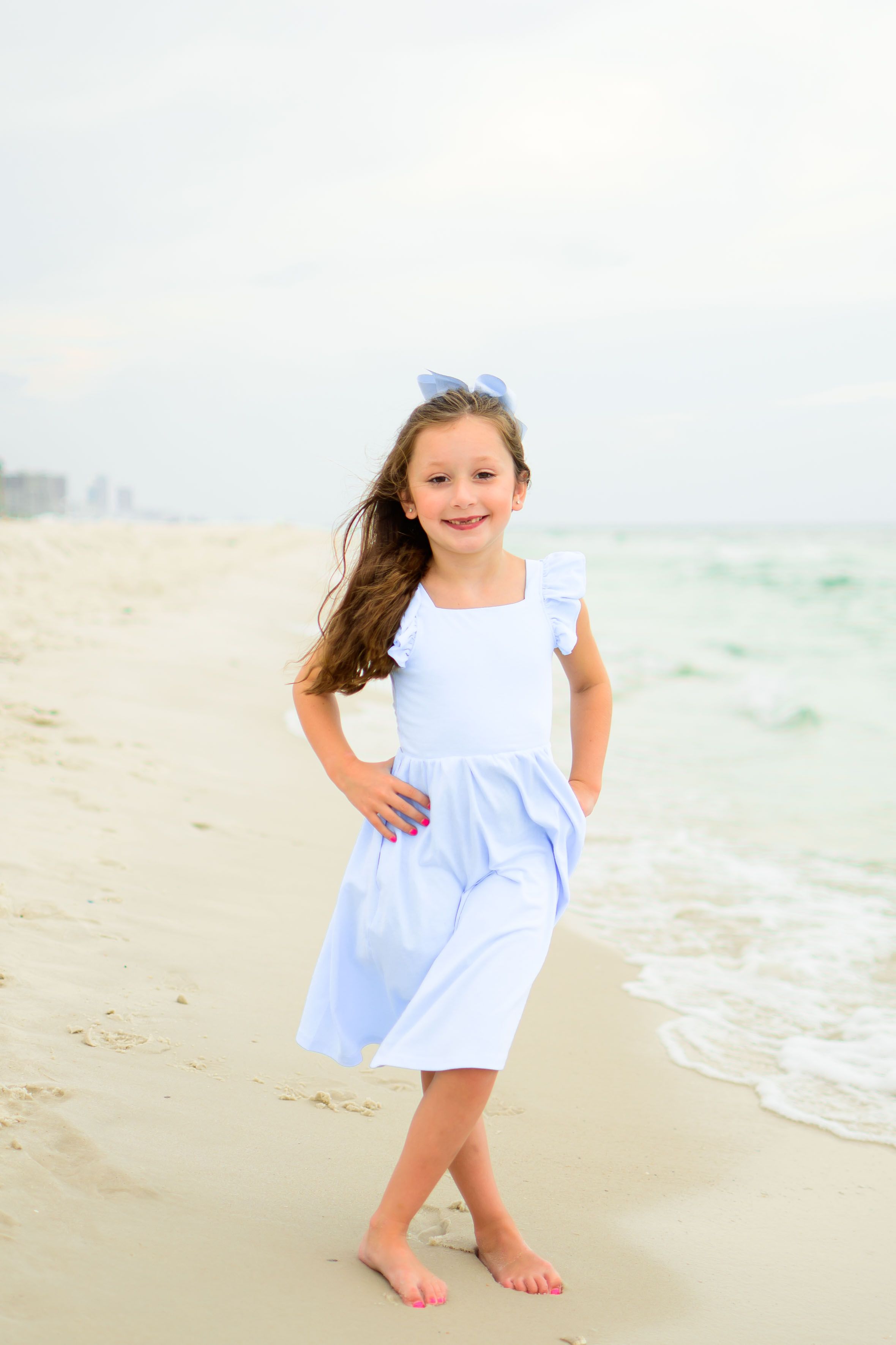 Young girl in a light blue dress poses happily on the beach.