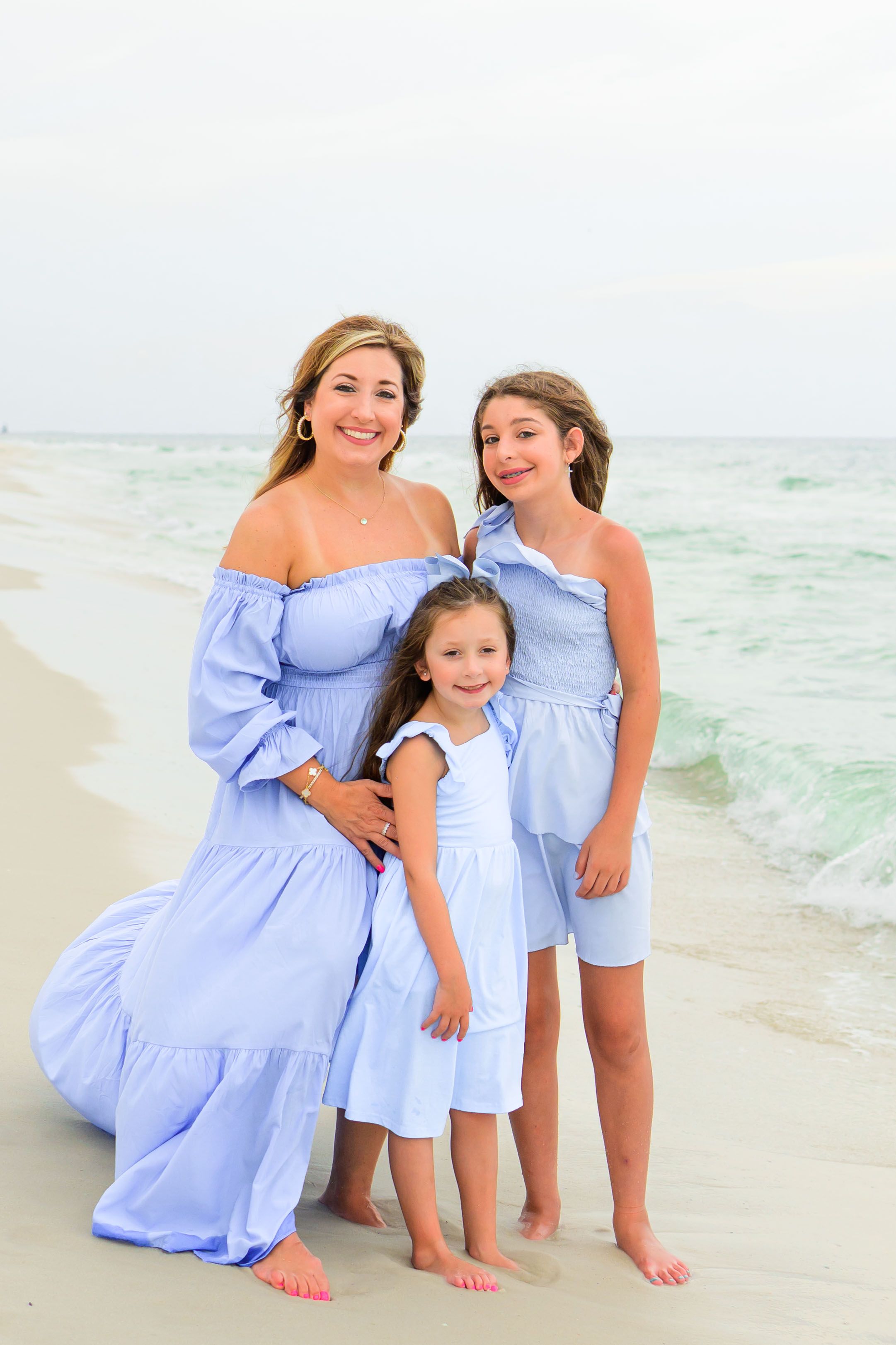 Three people in coordinating blue outfits pose together on a beach.