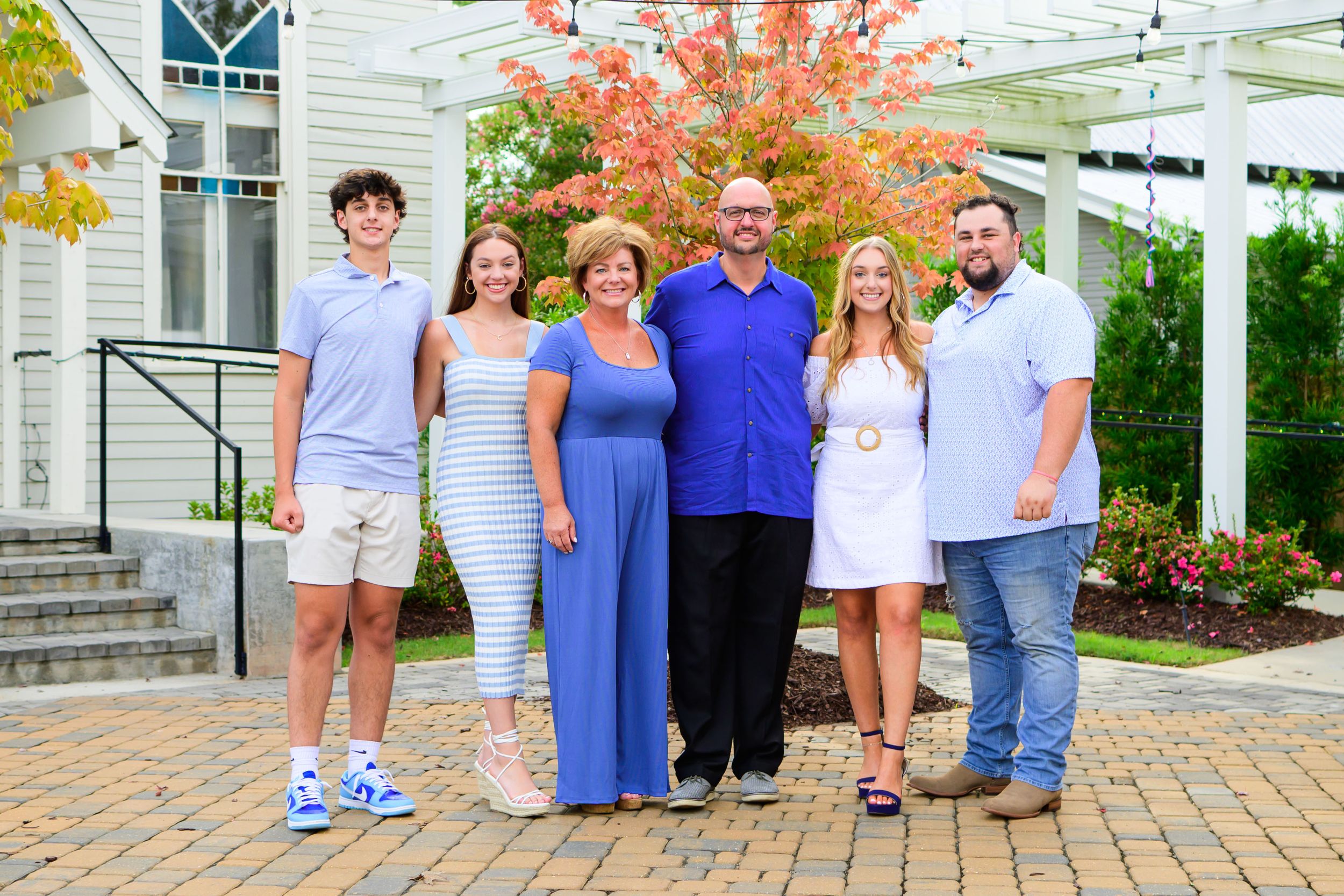 A group photo on a brick patio with colorful fall foliage and a white church building behind them.