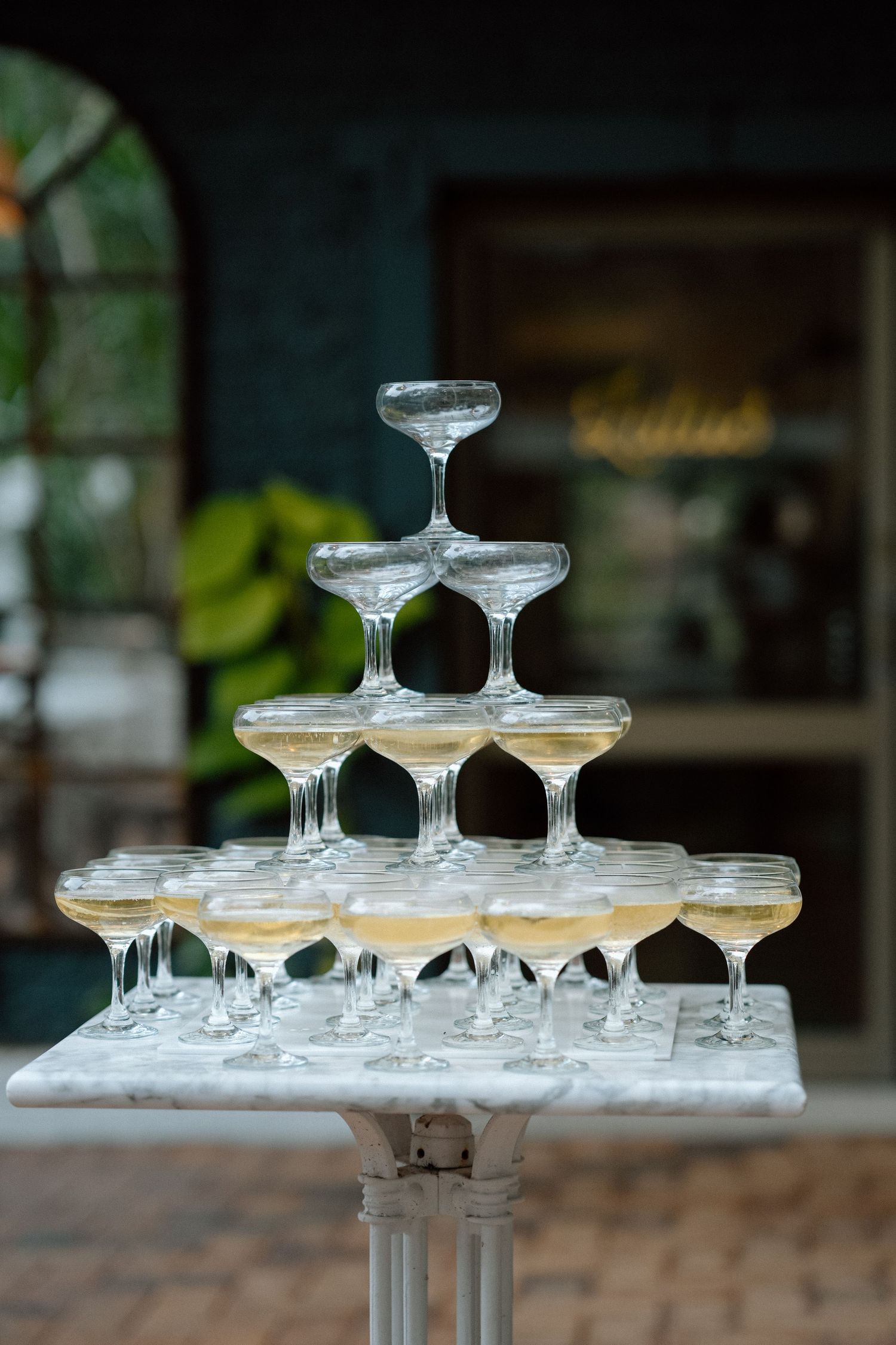 Elegant champagne tower with coupe glasses stacked in pyramid formation on white pedestal.