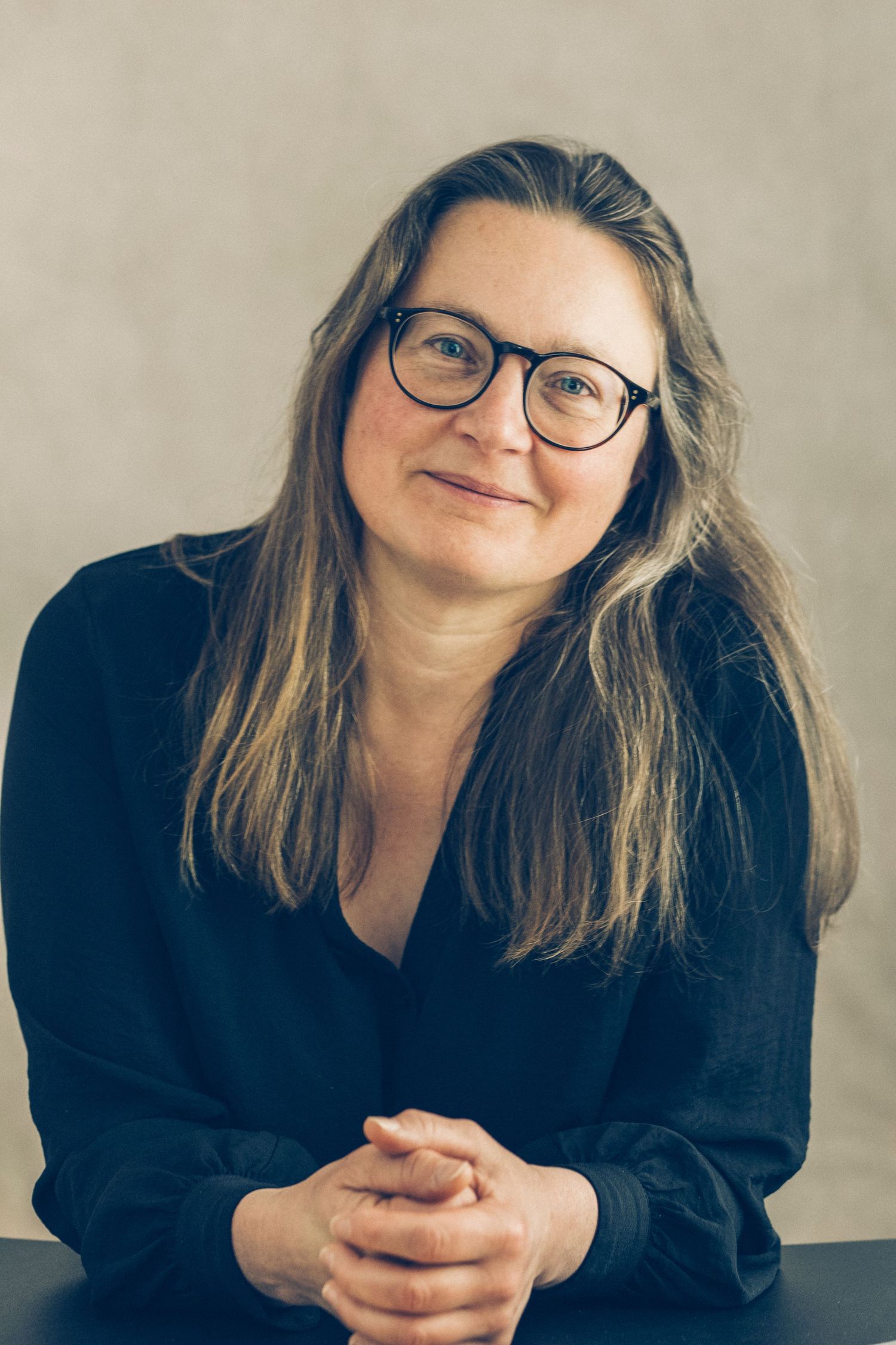 Portrait einer langhaarigen Frau mit Brille schmunzelnd mit den Händen vor sich aufgestützt im Fotostudio Aurelia Schulz Bad Arolsen