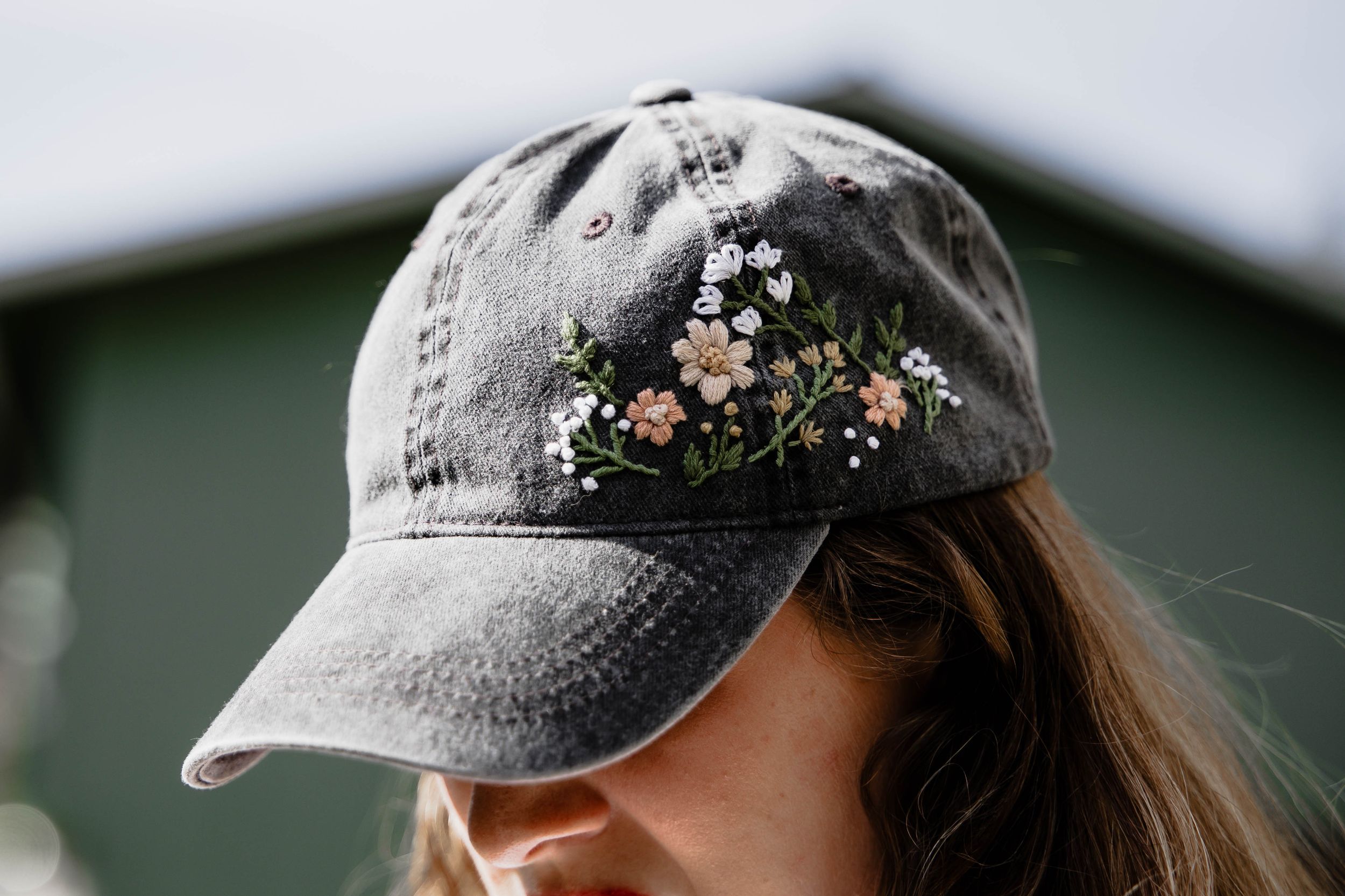Gray baseball cap with delicate floral embroidery detail shown in profile against a blurred background.