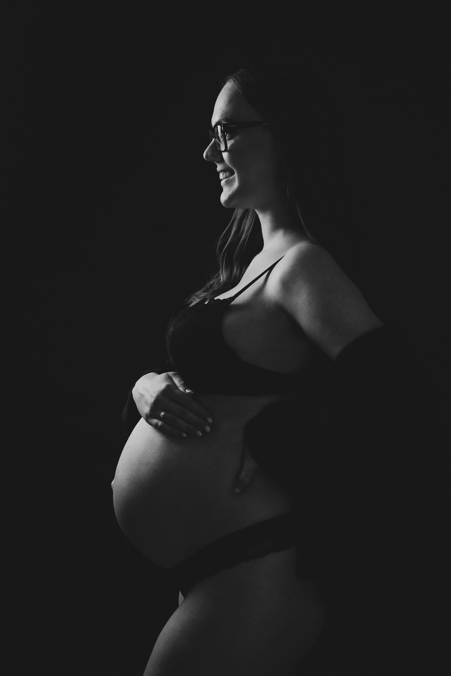 Intimate black and white maternity boudoir photo with dramatic side lighting.