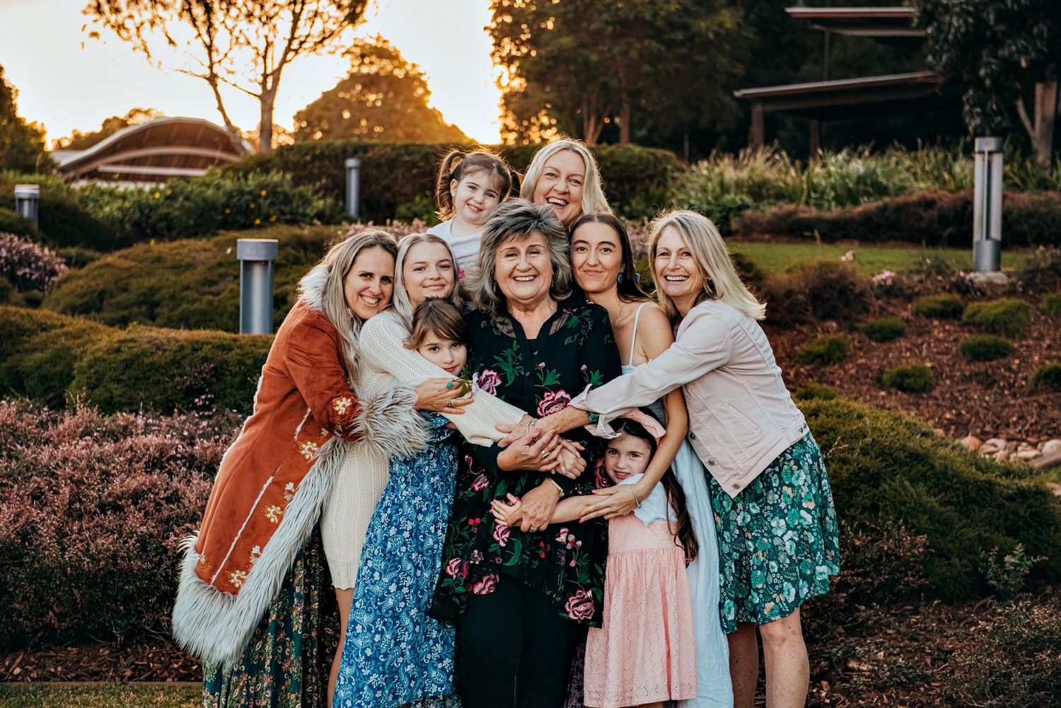 Joyful group photo of wedding party members in coordinated blue and pink outfits at sunset.