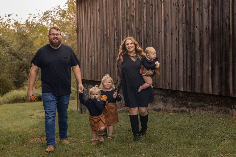 Family members walk together in front of a rustic wooden barn during an autumn photo session.
