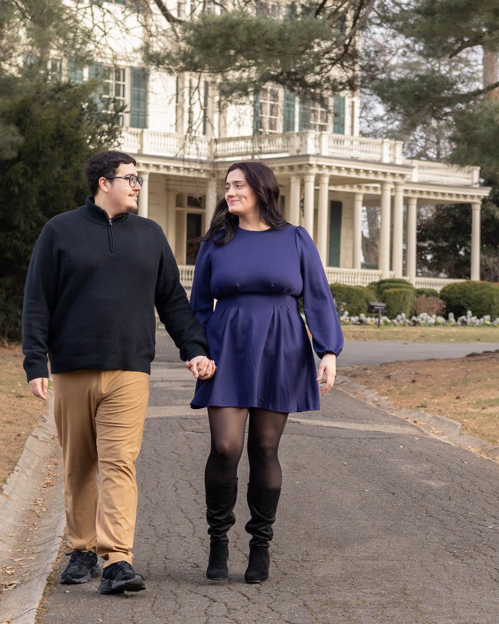 A couple walking together on a path near a grand historic building in fall weather.