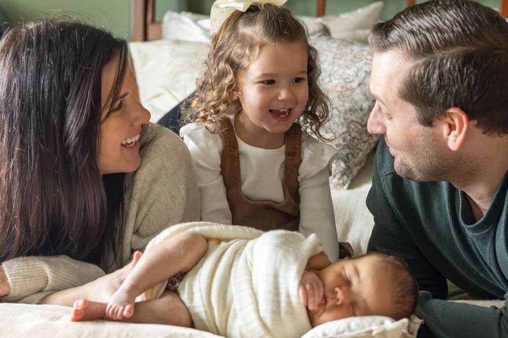 A happy family sharing a tender moment together while lying on a bed with a cream colored blanket.
