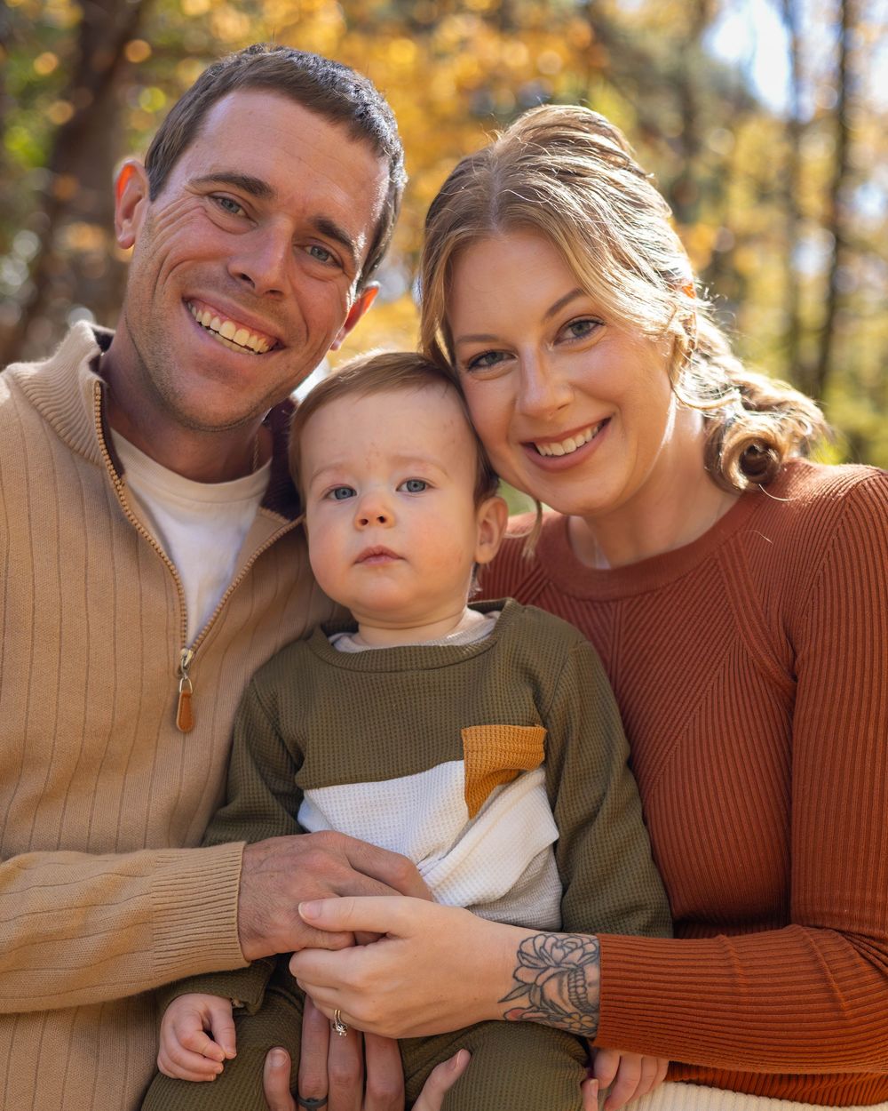A family shares tender moments together during an autumn outdoor photoshoot with golden bokeh lighting in the background.