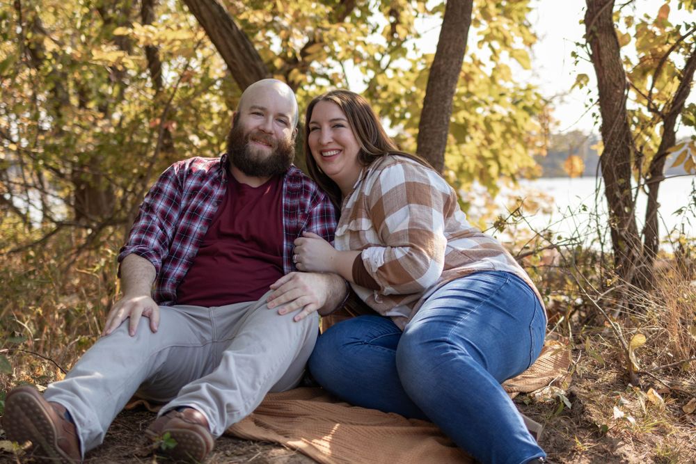 Couple sitting together and laughing on blanket during autumn outdoor photoshoot.