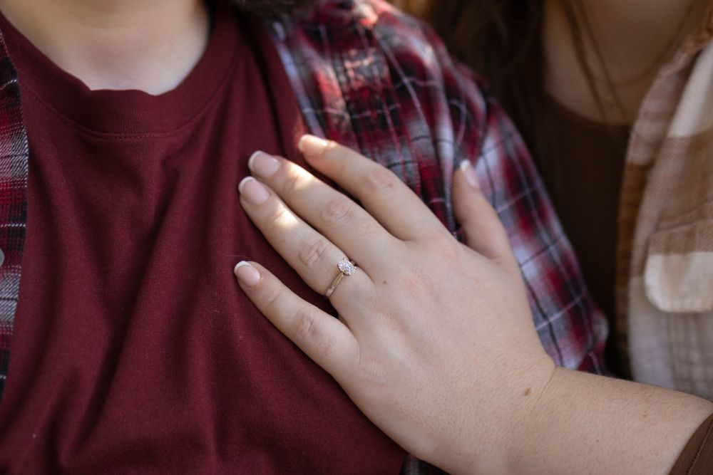 Close up of engagement ring on hand against plaid shirt.