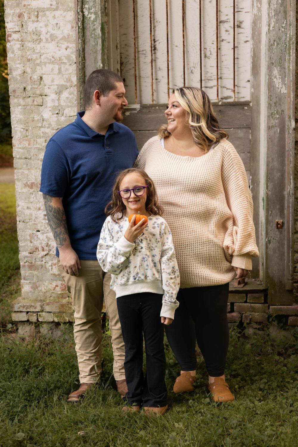 A family shares candid laughs together during an outdoor photo session against a rustic brick wall.
