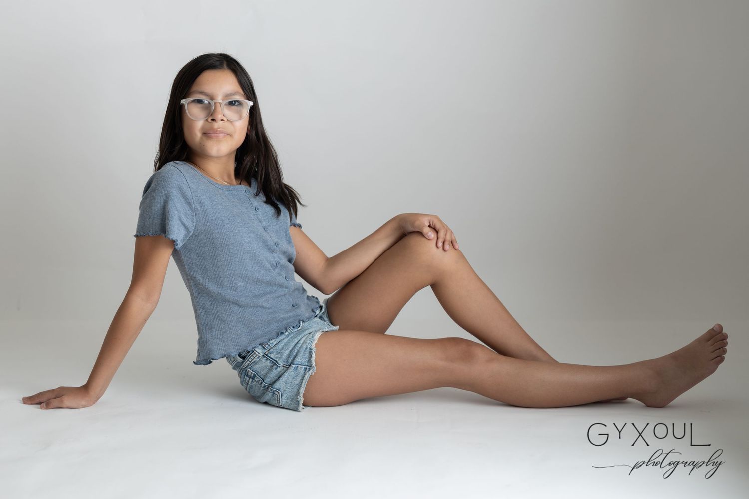 A casual photoshoot featuring a person in denim shorts and blue top lounging on a light background.