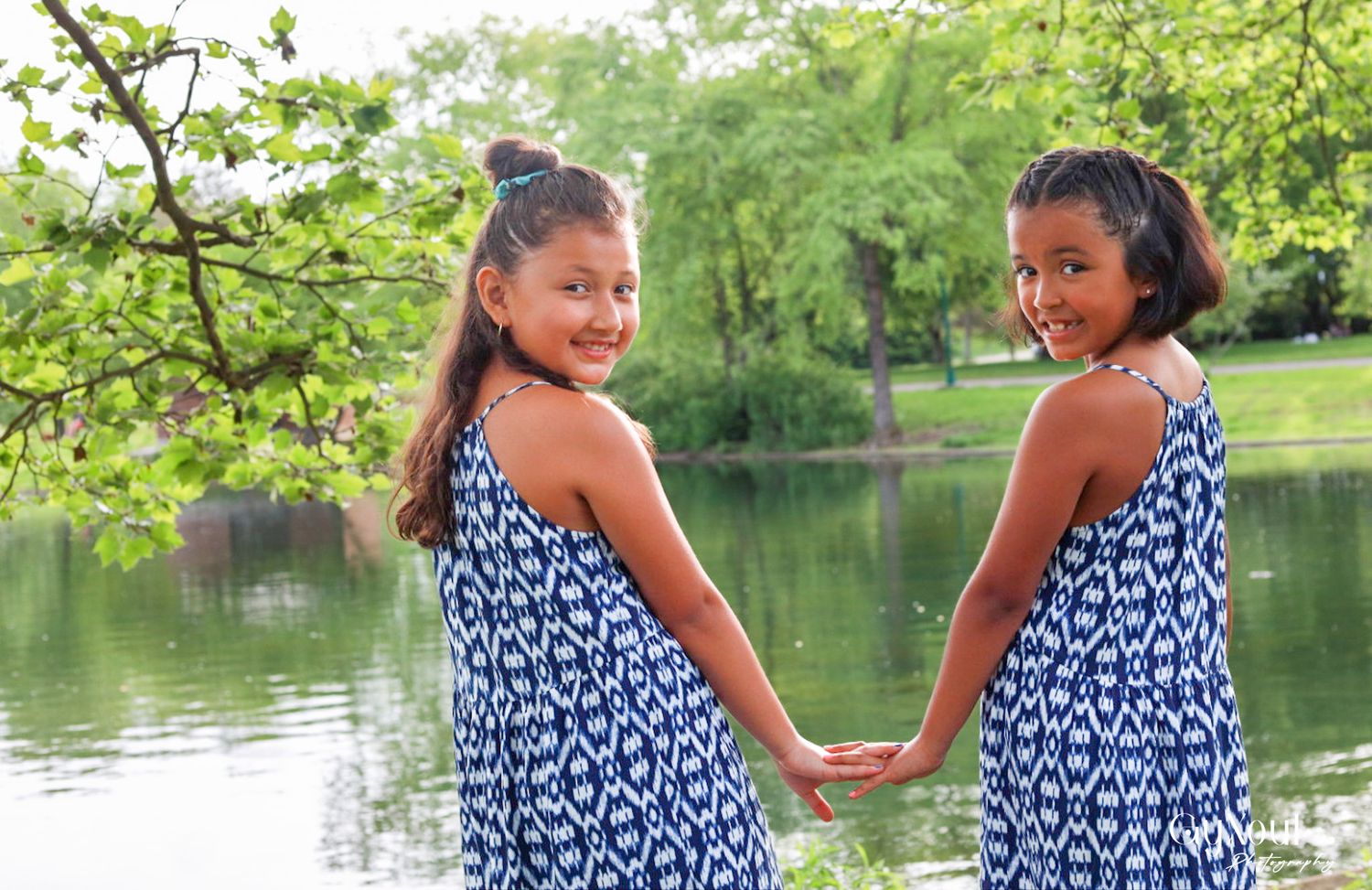 Two people in matching blue patterned dresses hold hands by a lake.