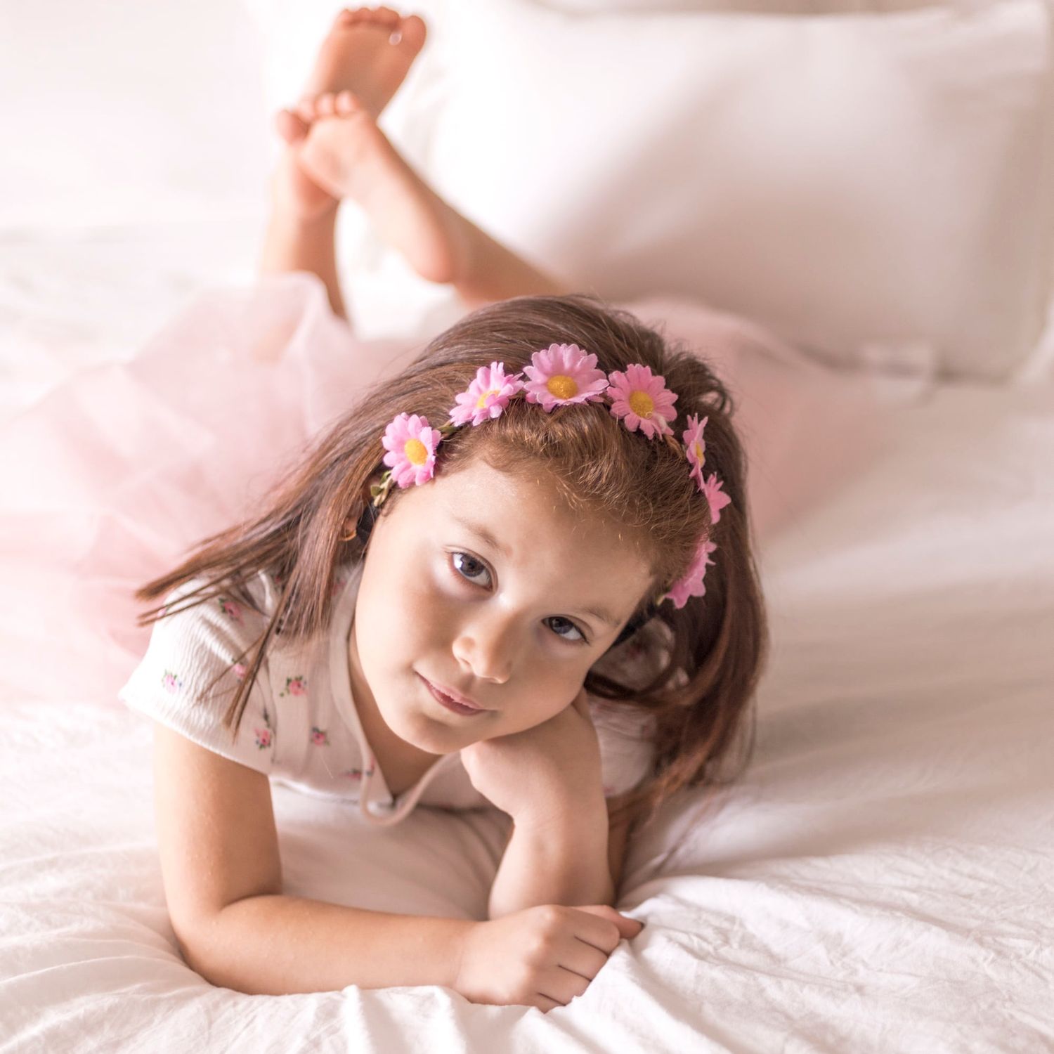 A dreamy portrait with pink flower crown and soft lighting on white bedding.