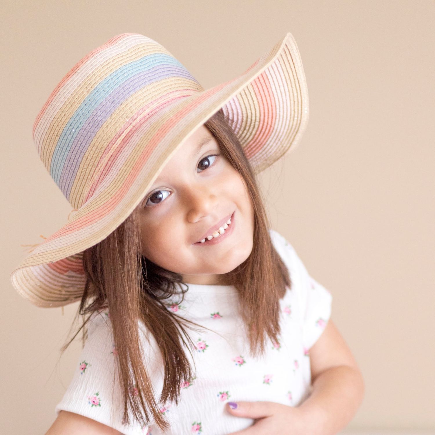 A portrait featuring a striped pastel sun hat and floral print dress against a neutral background.
