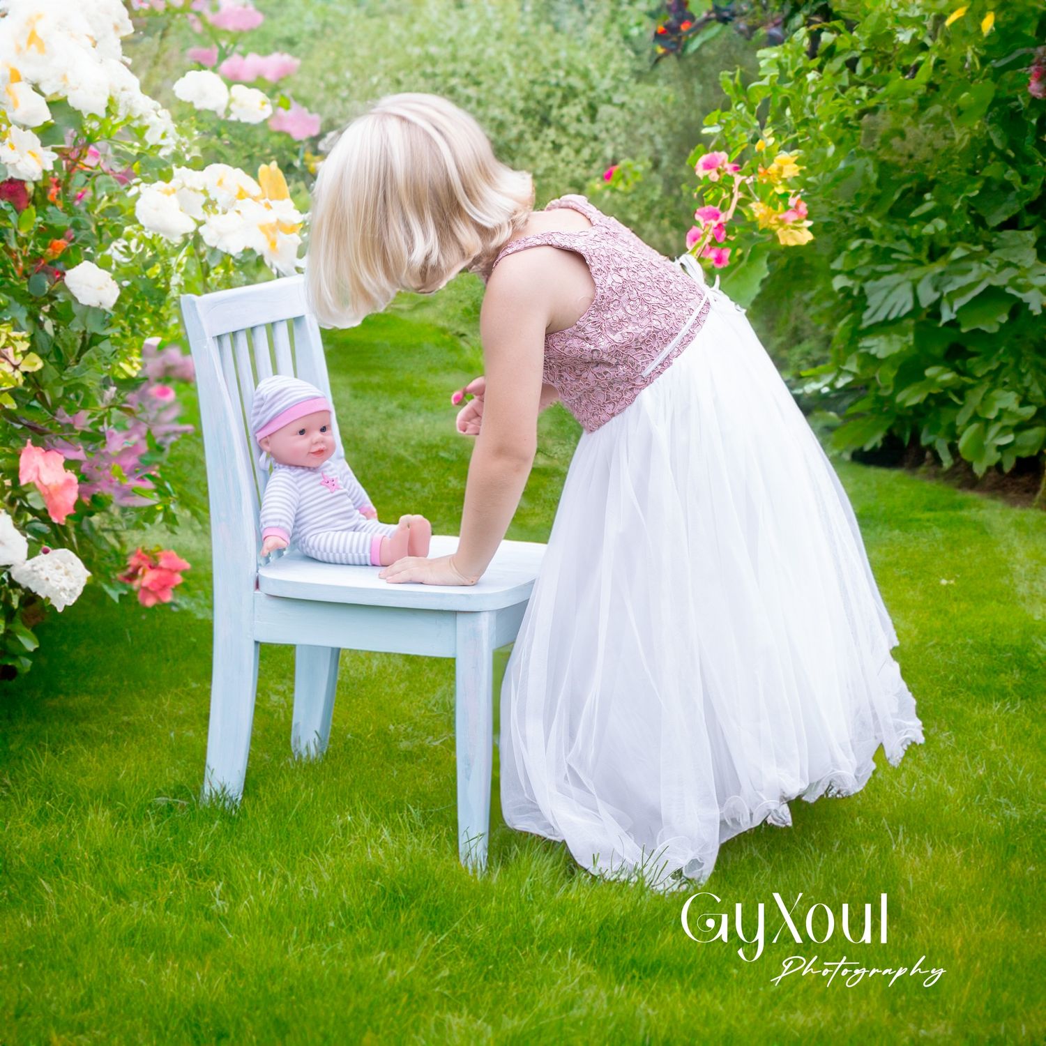A tulle dress-wearing figure bends over a blue chair in a flowering garden.