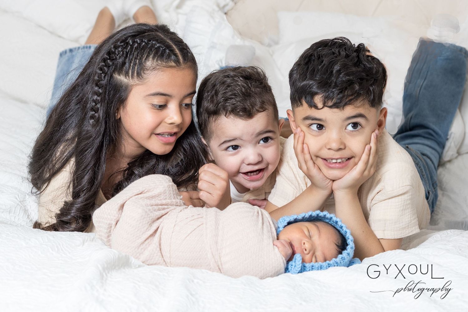 Three siblings sharing joyful moment together while lying on white bedding.