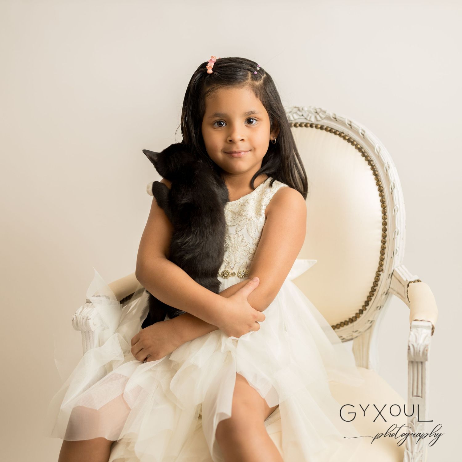 Portrait of a young person in a white tulle dress sitting on an elegant vintage chair.