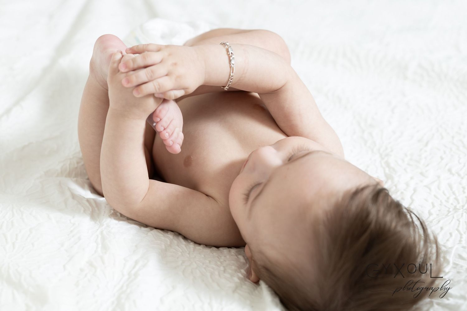 Sweet portrait of an infant lying on white bedding in natural light.