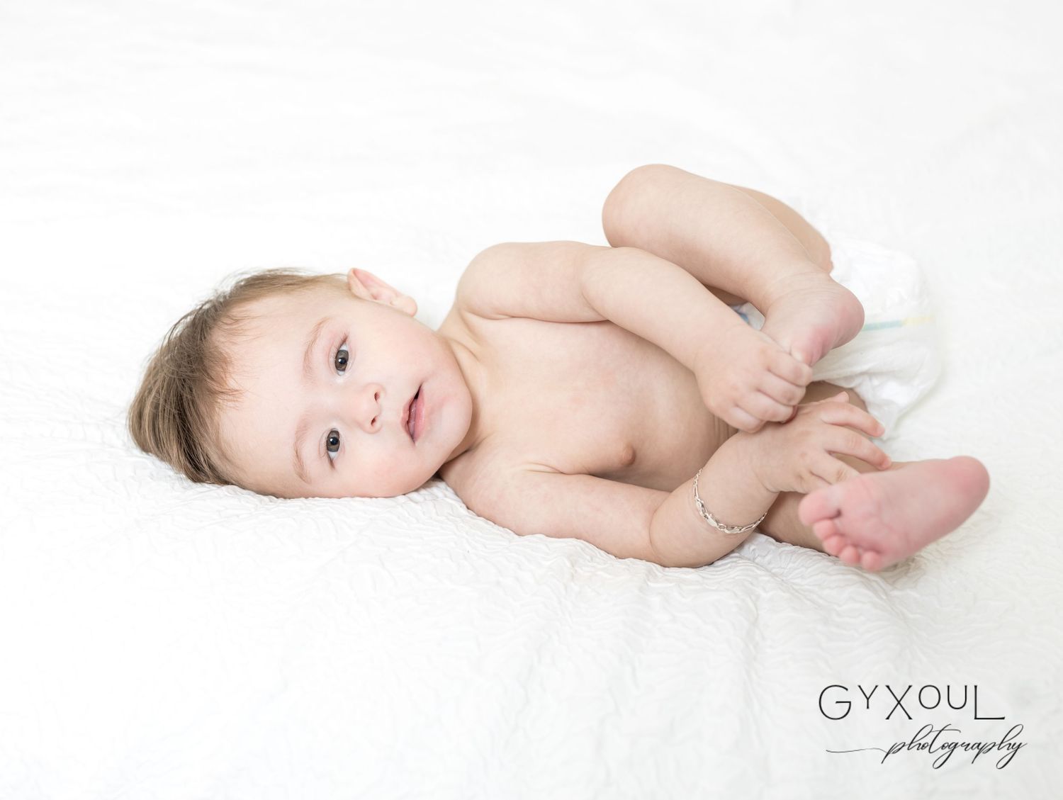 Natural newborn portrait with baby lying on soft white fabric.