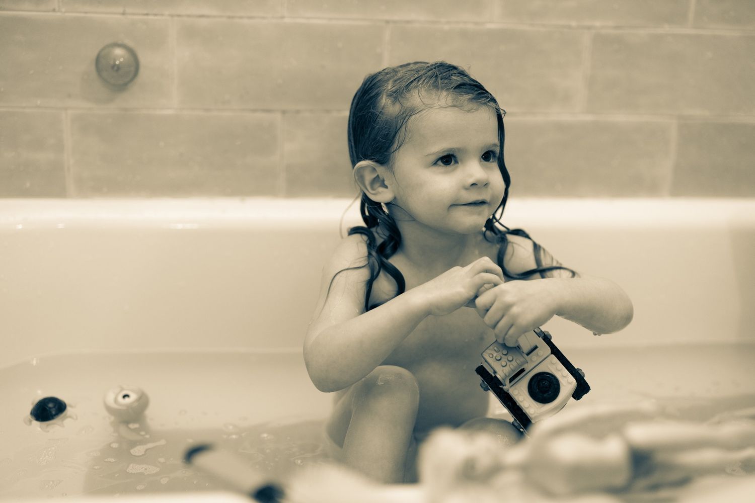Child playing with camera during bath time in vintage-style photograph.