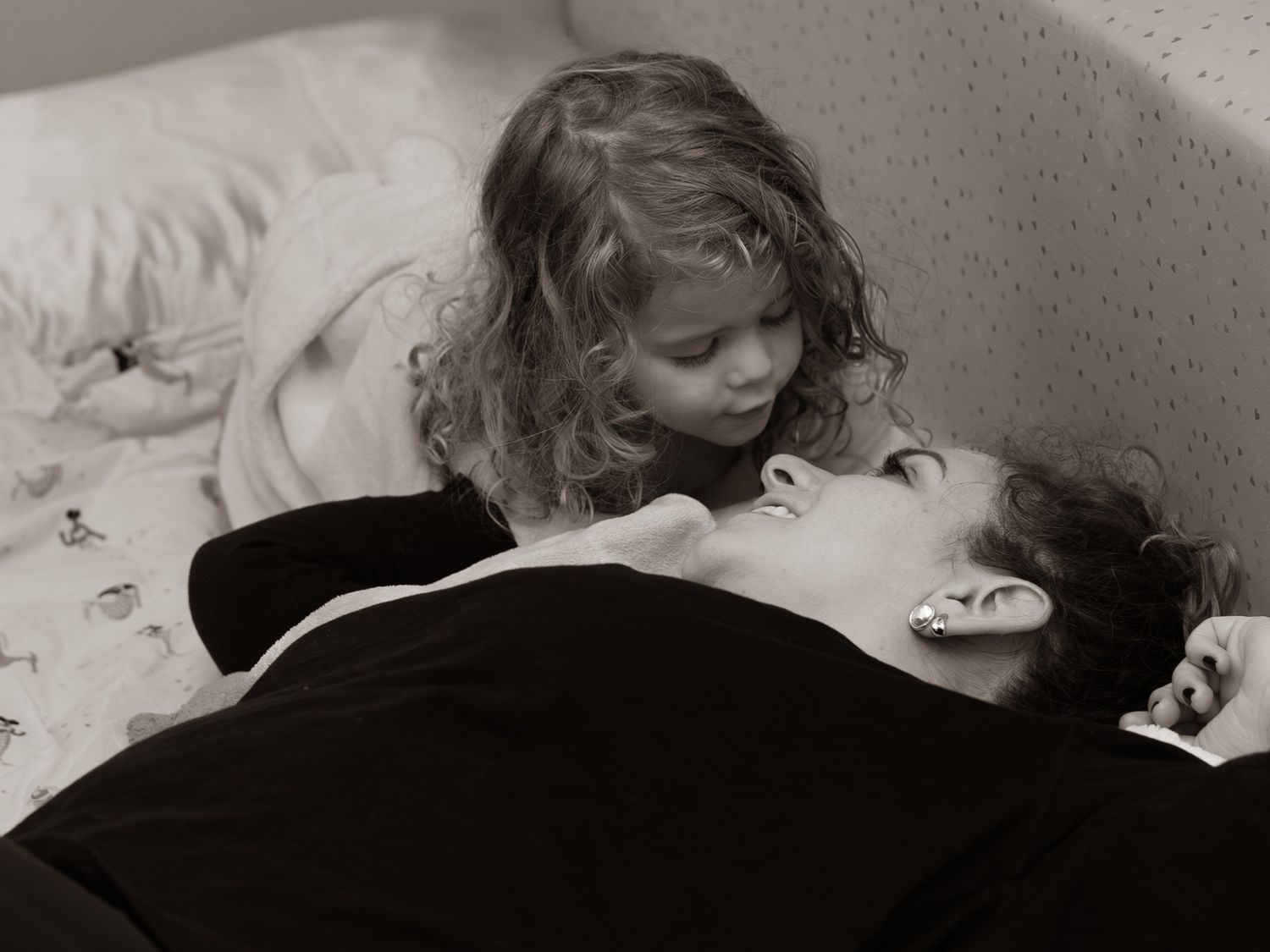 A tender black and white moment showing parent and child lying together on a bed.