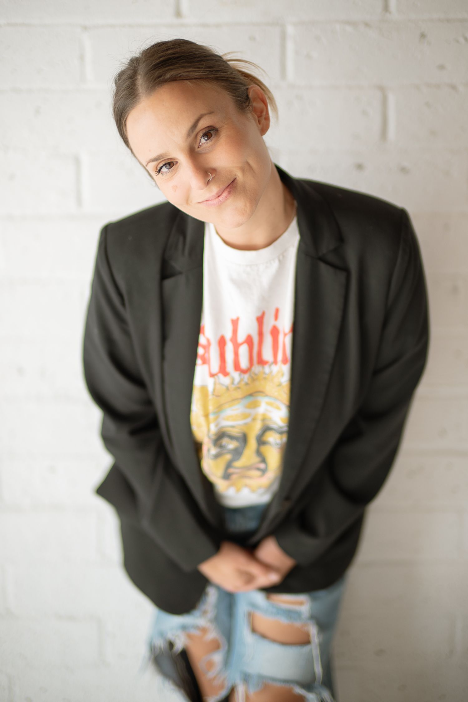 Artistic portrait series showing relaxed poses in black blazer and vintage t-shirt against white wall.
