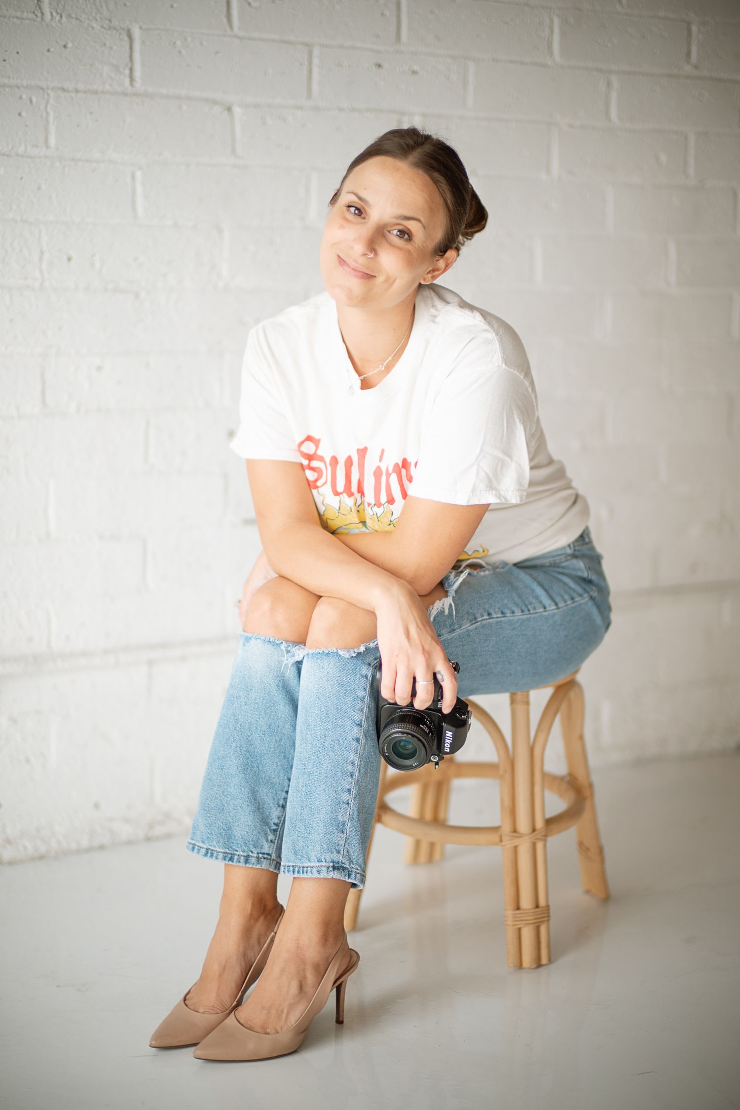 Studio portrait series showing casual poses on wooden stool against white brick wall.