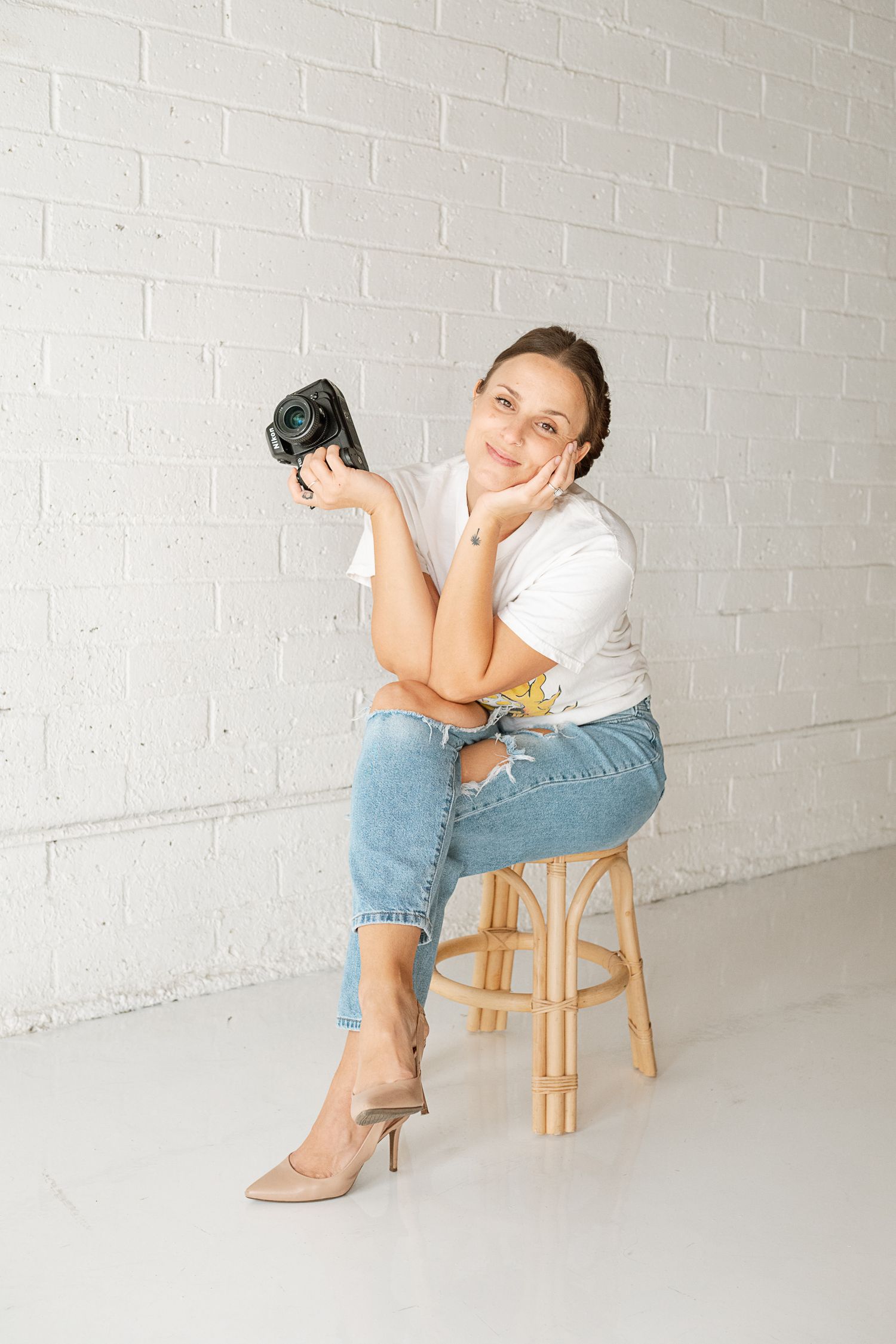 Creative portrait session with camera props and casual styling in minimalist studio setting.