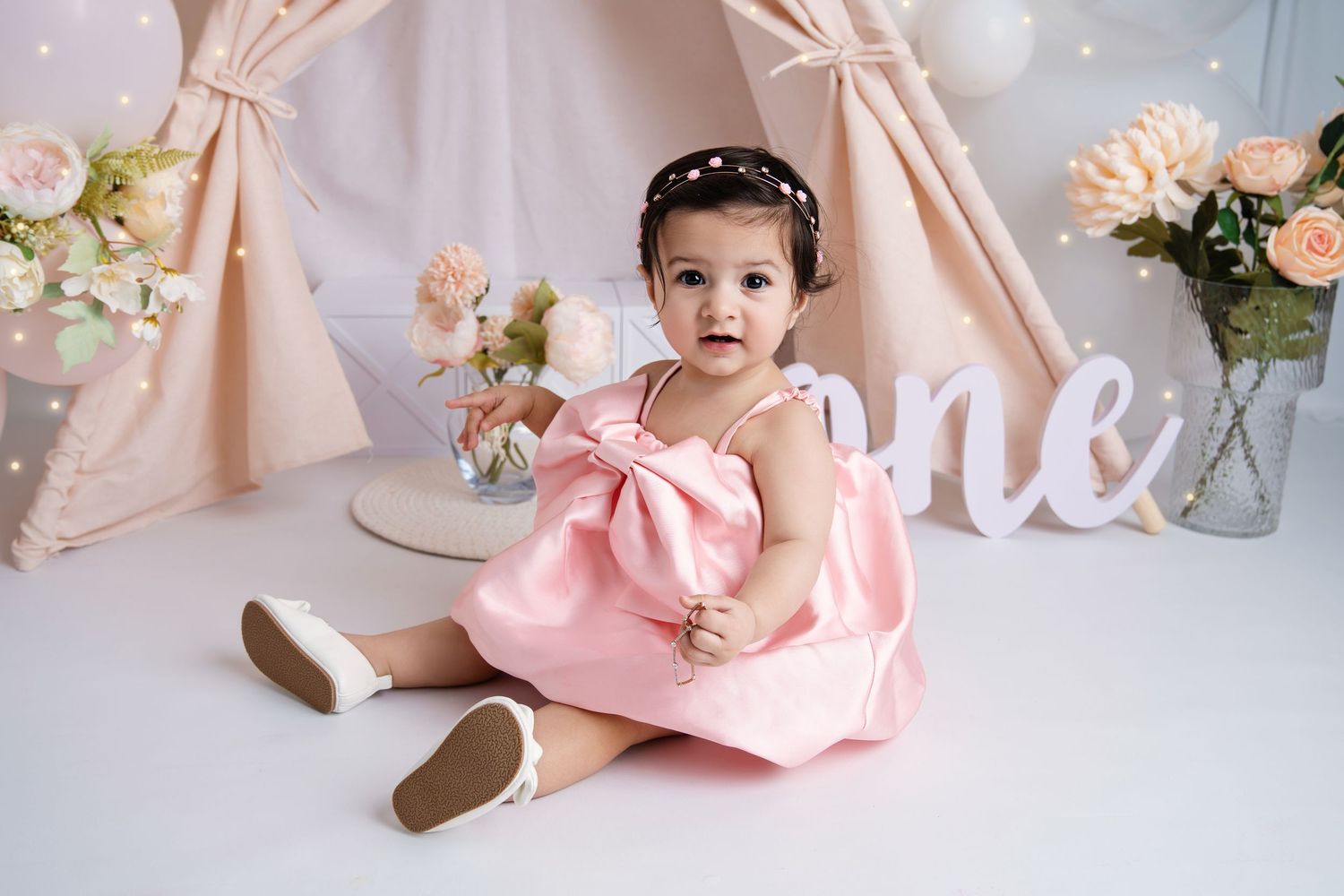 Pink and white cake smash photo setup with floral decorations and balloons for first birthday celebration.