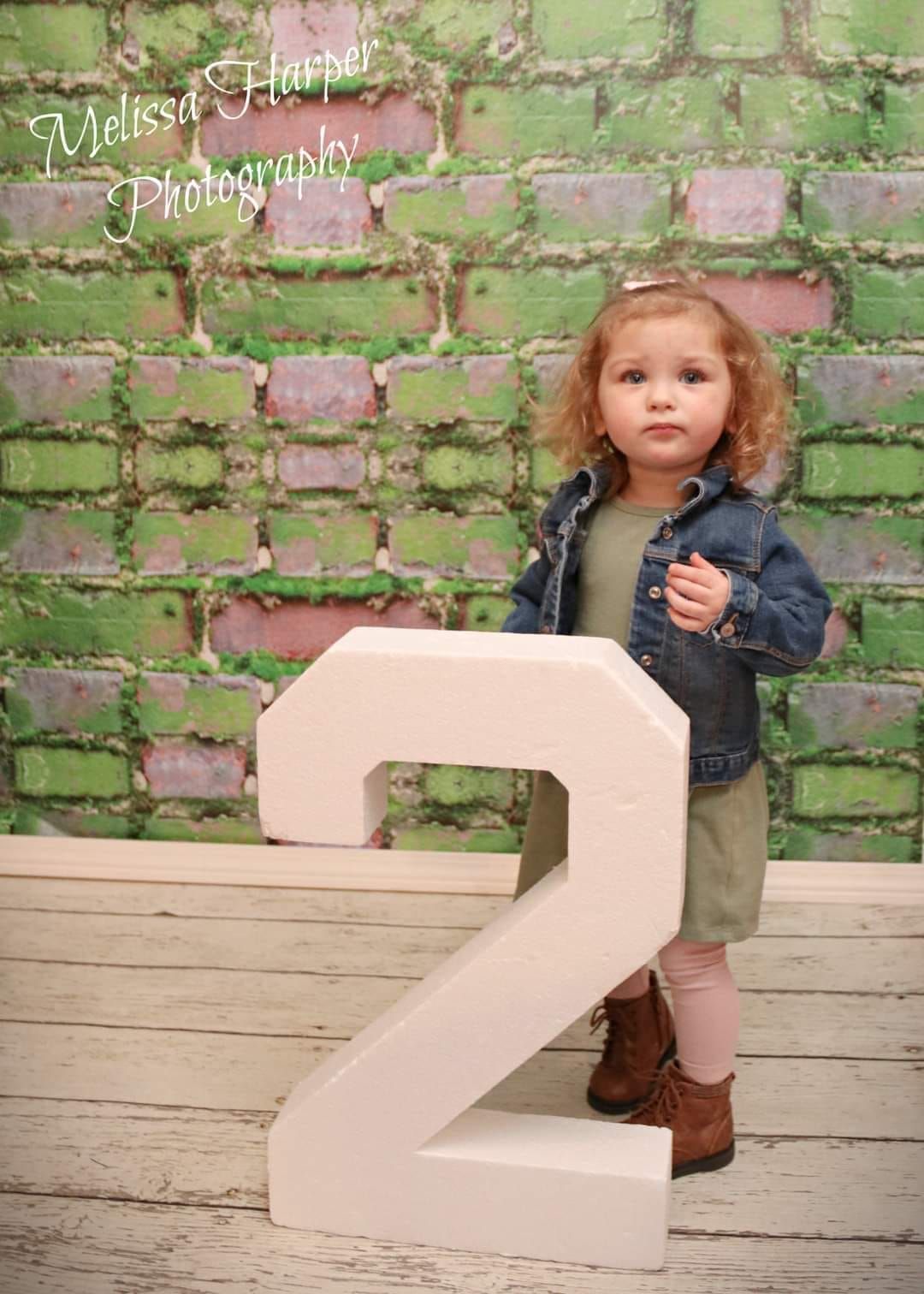 Photography setup with large decorative number 2 prop against green brick wall backdrop.
