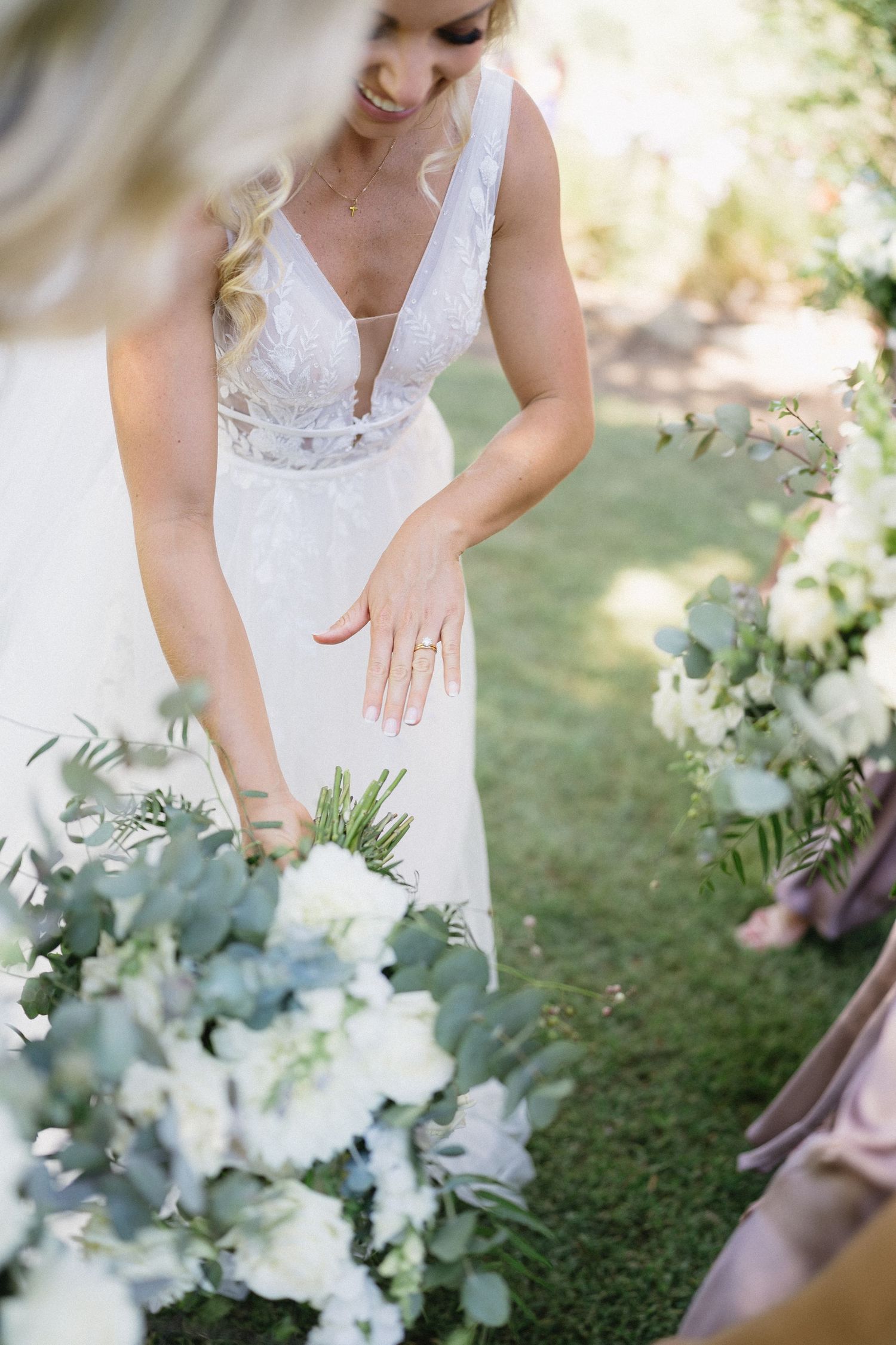 Close up of bridal gown details and white floral arrangements at outdoor wedding.