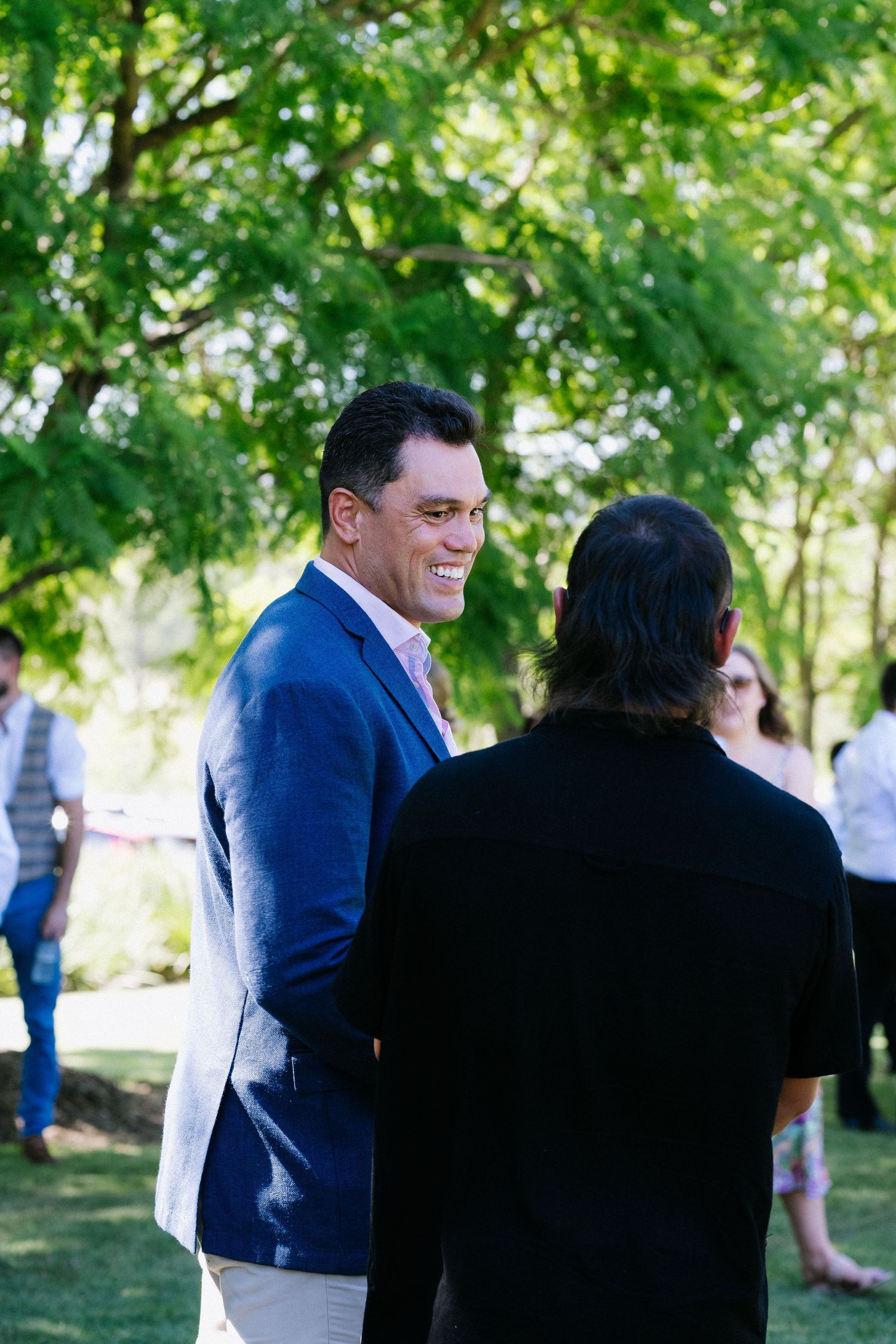 Wedding guest in a navy suit smiles during outdoor garden reception.