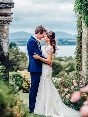 Romantic wedding couple embracing in garden with mountain lake view and blooming roses.