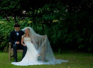 A romantic forest wedding photography session shows a couple in formal attire resting on lush green grass.
